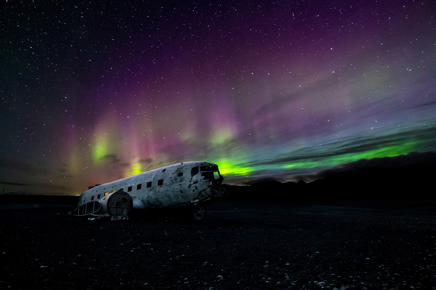 Polarlichter erhellen den Himmel über einem DC-3 Flugzeugwrack in Islands Süden. 